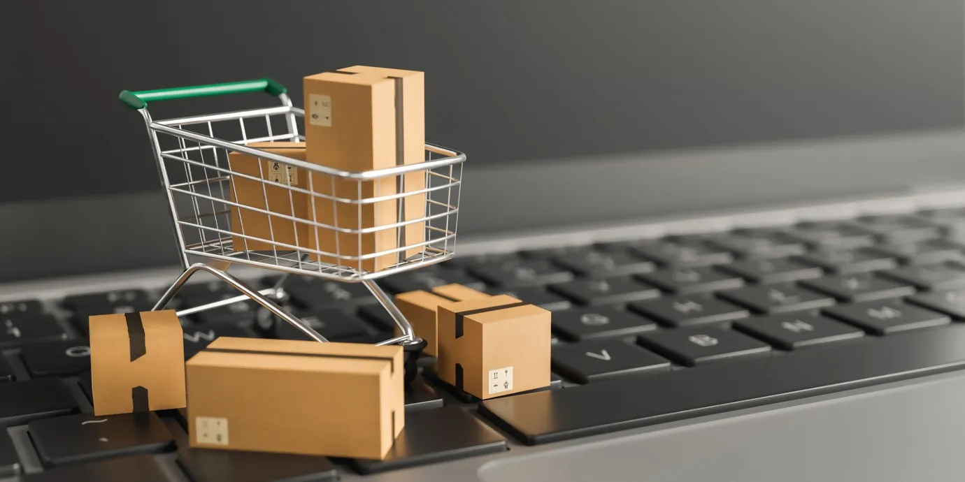 A shopping trolley on a computer keyboard, filled with small parcels.