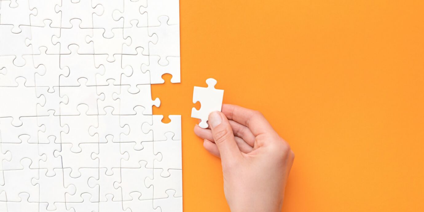 Letztes weisses Puzzleteil wird von Hand ergänzt, Puzzle auf orangem Hintergrund