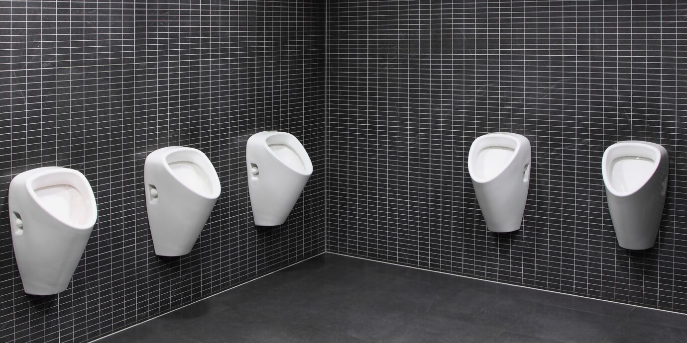 Mehrere weisse Urinale an Wand mit kleinen, schwarzen Platten