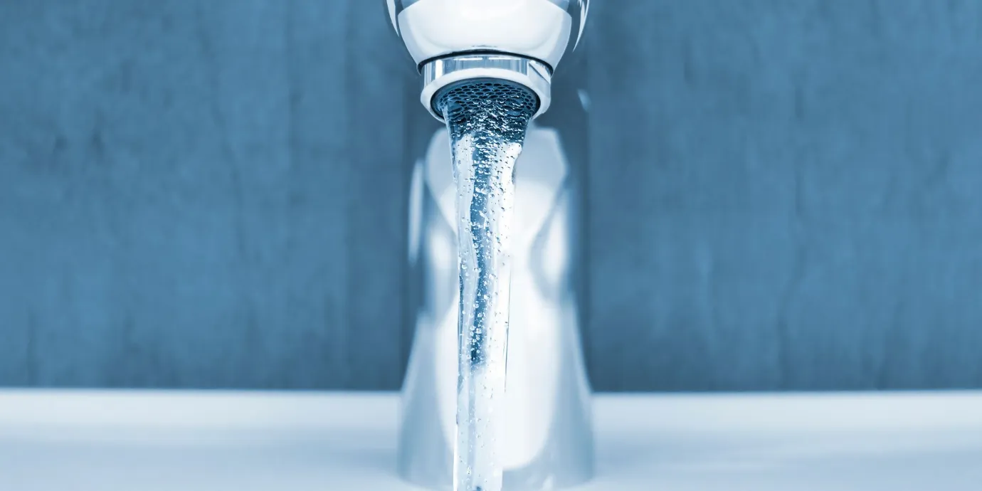 Close-up of modern washbasin tap with running water in front of blue wall and white washbasin