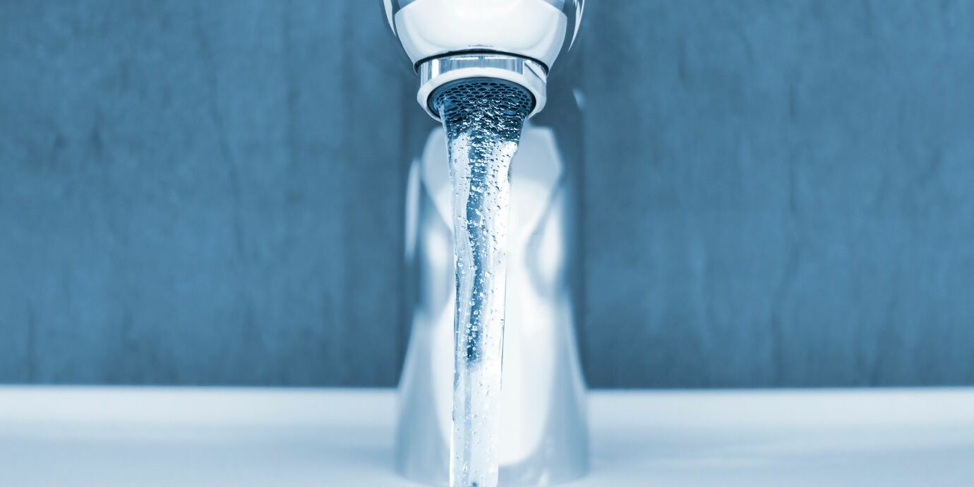 Nahaufnahme moderne Waschtischarmatur mit fliessend Wasser vor blauer Wand und weissem Lavabo