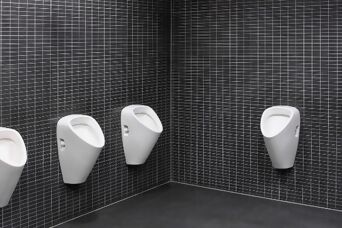 Mehrere weisse Urinale an Wand mit kleinen, schwarzen Platten