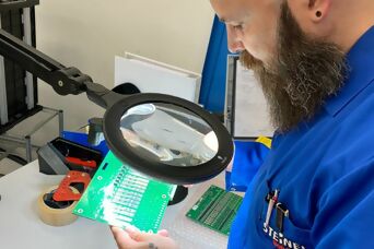 ein Mitarbeiter hält bei der Warenausgangskontrolle eine Leiterplatte unter ein Vergrösserungsglas