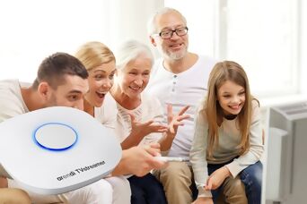 Auracast™ TV Streamer gross dargestellt, im Hintergrund fünf Personen unterschiedlich alt, die alle in die gleiche Richtung schauen und sich freuen