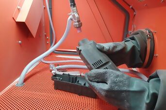 Einblick in 3D-Drucker bzw. Strahlkabine, Reinigung 3D-Druckteil mit schwarzen Handschuhen
