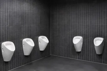 Mehrere weisse Urinale an Wand mit kleinen, schwarzen Platten