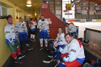 Eine lachende Gruppe in Eishockey-Ausrüstung neben dem Eis bei der Pause