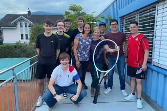 10 Personen posieren mit einem riesen grossen Squashracket für ein Gruppenfoto