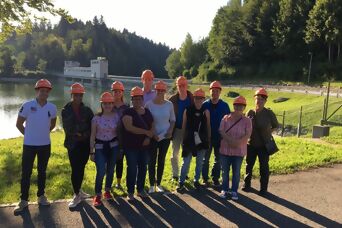 Eine Gruppe von Personen mit Schutzhelmen vor der Staumauer