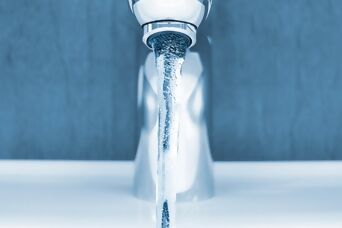 Close-up of modern washbasin tap with running water in front of blue wall and white washbasin