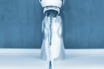 Nahaufnahme moderne Waschtischarmatur mit fliessend Wasser vor blauer Wand und weissem Lavabo