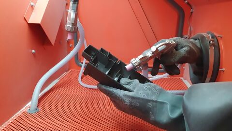 Einblick in 3D-Drucker bzw. Strahlkabine, Reinigung 3D-Druckteil mit schwarzen Handschuhen