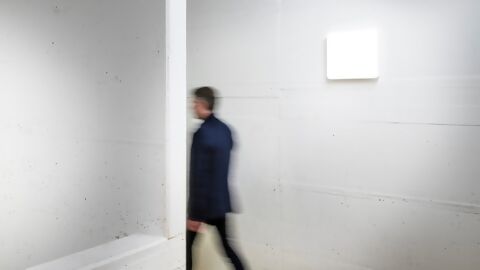 Person in Betontreppenhaus in Bewegung, löst Sensor in weisser, quadratischer Leuchte aus, Icon für Deckensensor auf orangem Kreis, links oben Icon für On-Off-Schalter und Tageslicht