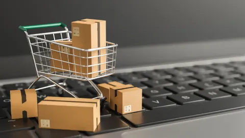 Einkaufswagen auf Computertastatur mit kleinen Paketen.
