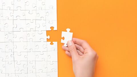Letztes weisses Puzzleteil wird von Hand ergänzt, Puzzle auf orangem Hintergrund