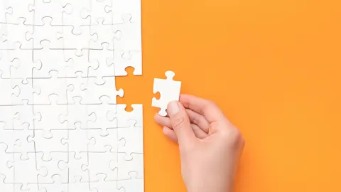 Letztes weisses Puzzleteil wird von Hand ergänzt, Puzzle auf orangem Hintergrund
