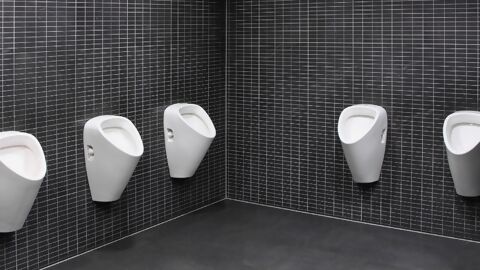 Mehrere weisse Urinale an Wand mit kleinen, schwarzen Platten
