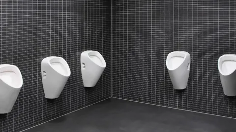 Mehrere weisse Urinale an Wand mit kleinen, schwarzen Platten