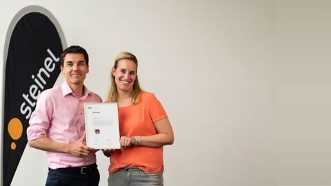 Marco Lang, CEO STEINEL Solutions und Melanie Niklaus, ehem. Head of Human Resources mit Urkunde von Fachstelle UND neben Steinel Beachflag