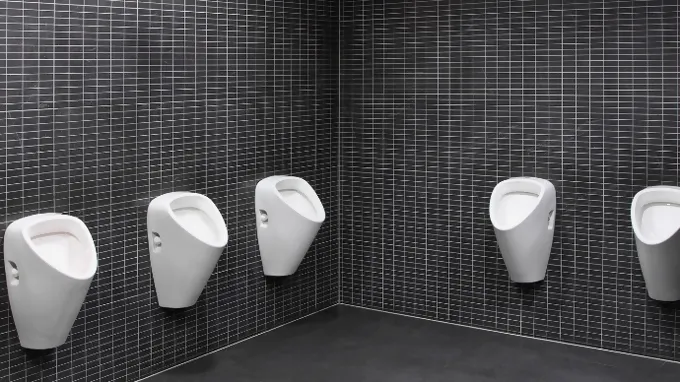 Several white urinals on the wall with small black plates