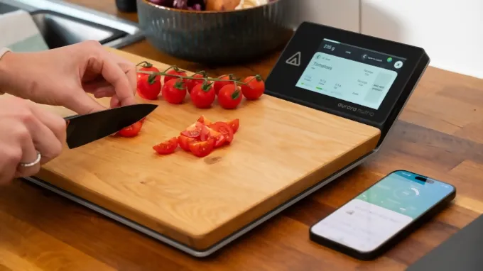 Aurora Nutrio cutting board with digital display and mobile device with app, a person cutting tomatoes on the cutting board.